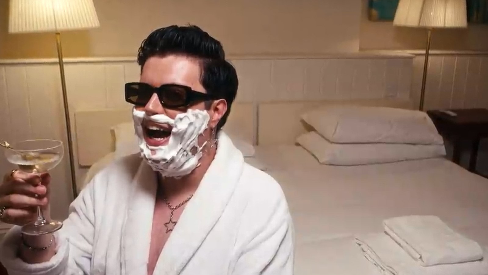 A man in a bathrobe with a face full of shaving foam, holding a martini