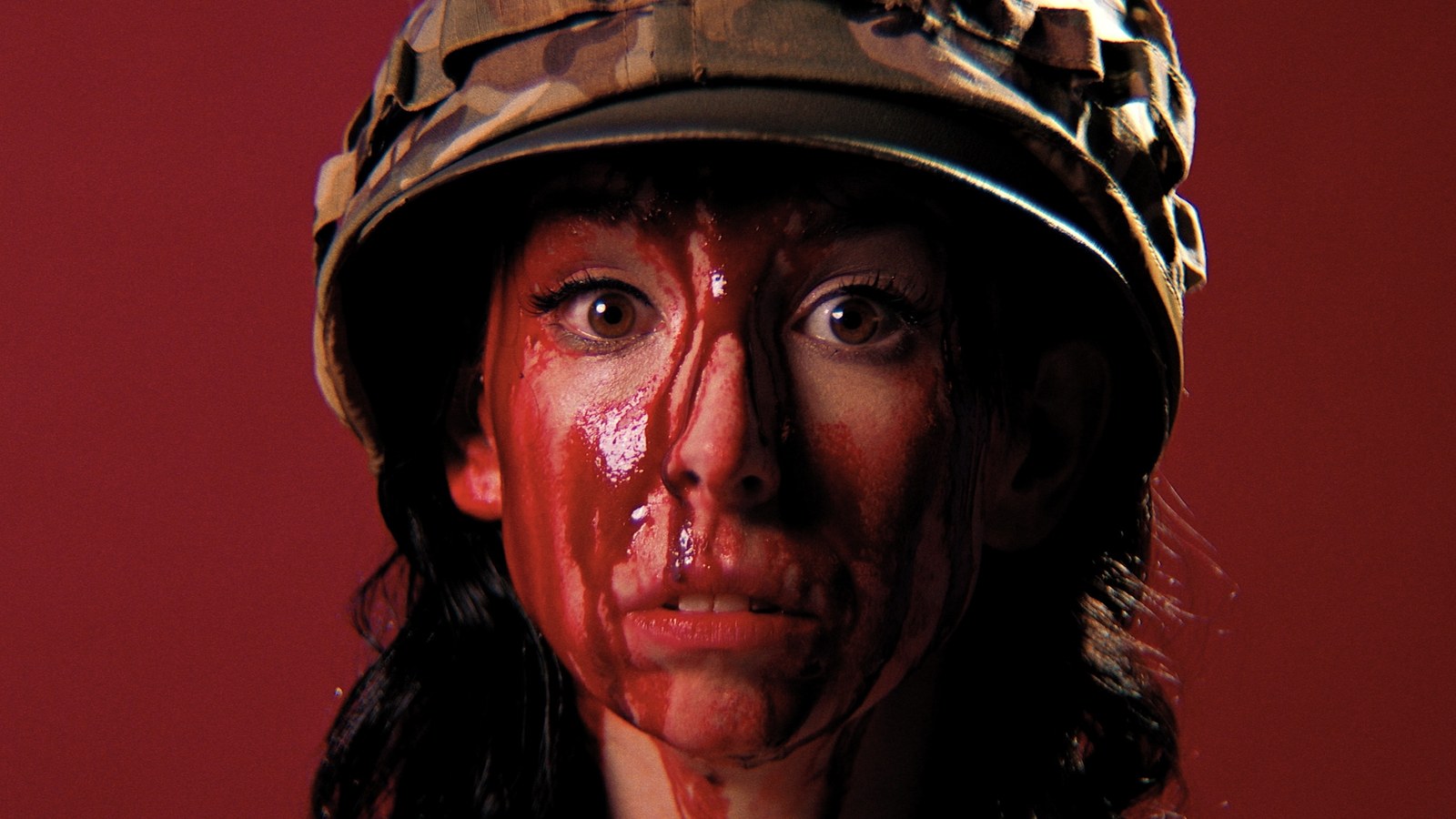 A bloodied soldier in a studded helmet against a red ground