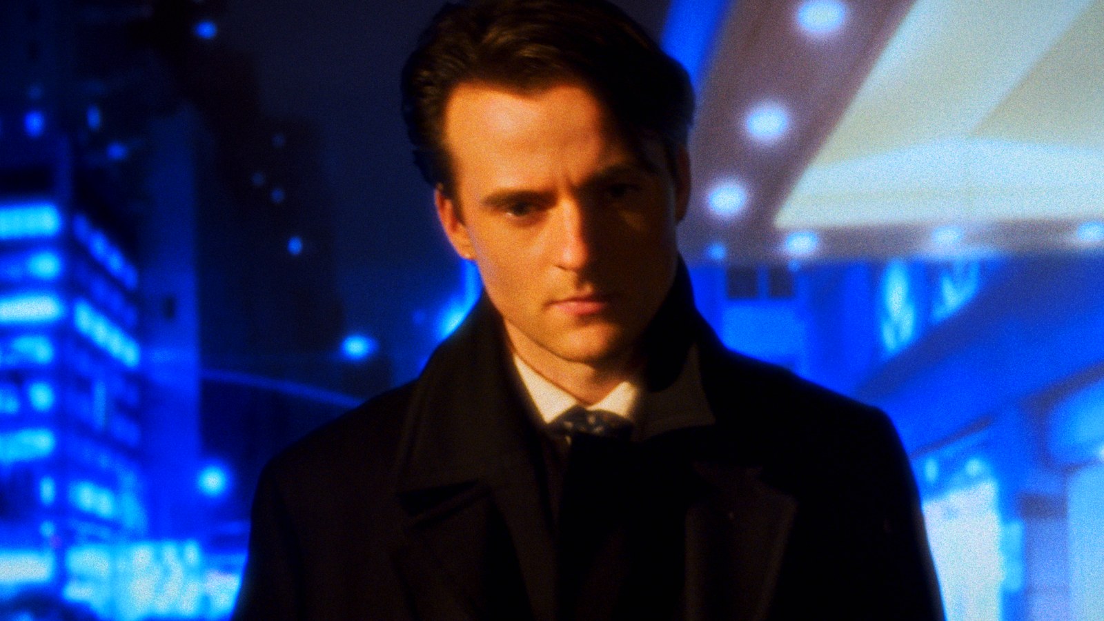 A man in a dark suit lit by blue neon
